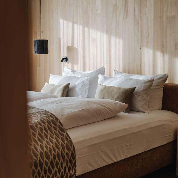 Gemütliches Schlafzimmer mit Holzverkleidung, großem Bett, vielen Zierkissen und gemustertem Überwurf.