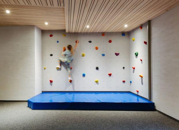Indoor-Kletterwand mit bunten Griffen und blauer Matte, an der ein Kind hinaufklettert.