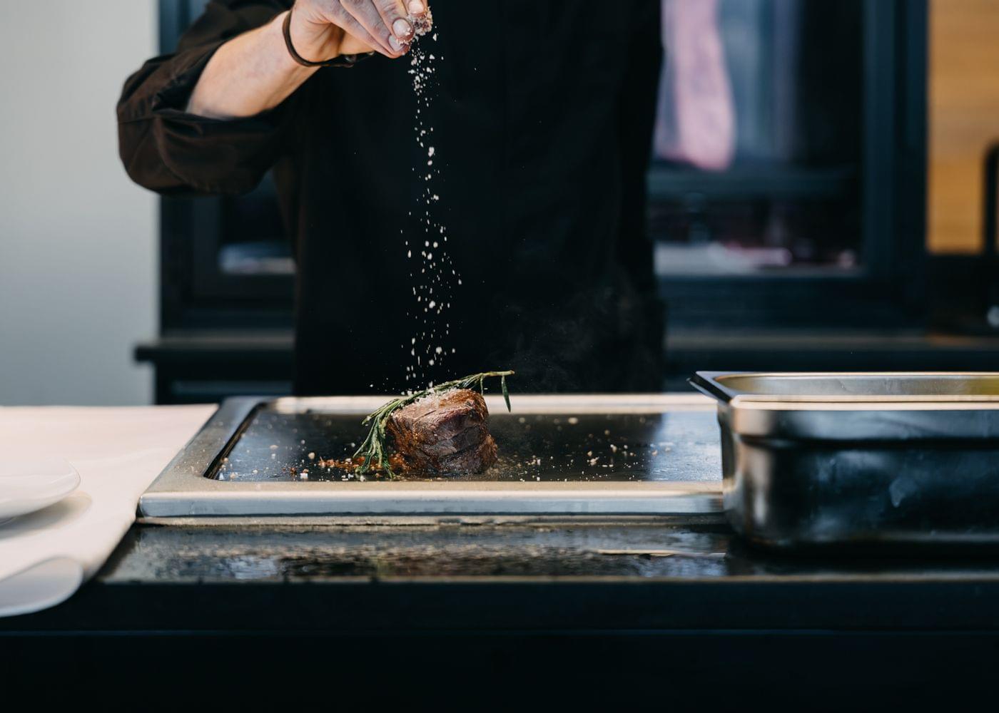 Koch streut Gewürze über ein Gericht an der Arbeitsfläche in einer modernen offenen Küche