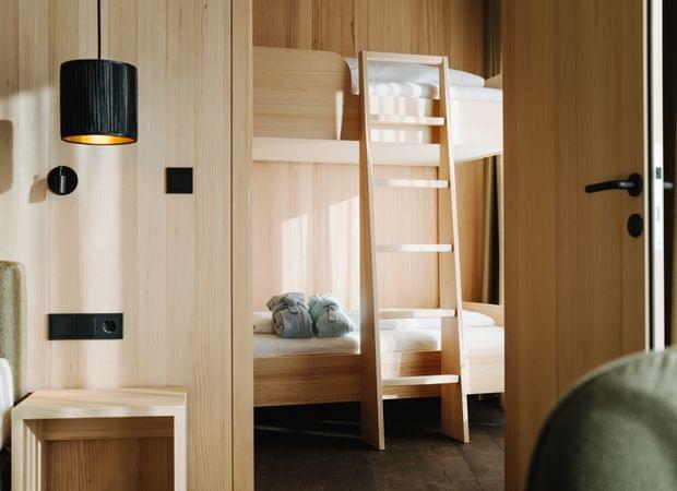 Blick in ein Kinderzimmer mit Holz-Stockbett, weißen Kissen und zwei gefalteten Bademänteln auf der unteren Liegefläche.