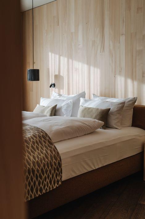 Gemütliches Schlafzimmer mit Holzverkleidung, großem Bett, vielen Zierkissen und gemustertem Überwurf.