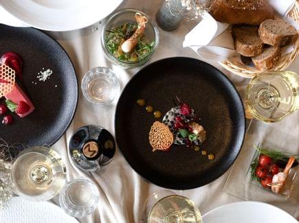 Mehrere Teller in schwarz und weiß mit Gerichten auf einem gedeckten Essenstisch - Torghele's Wald + Fluh