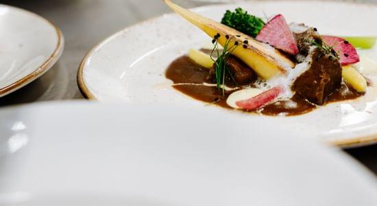 Mehrere fein angerichtete Gourmetgerichte stehen auf weiß gedecktem Tisch, eines davon scharf im Vordergrund