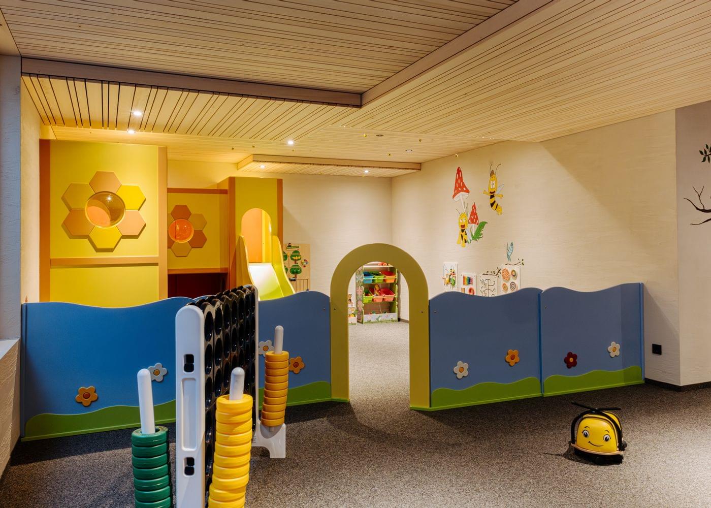 Bunter Indoor-Kinderbereich mit Spielwänden, kleinem Durchgangsbogen, Wandelementen in Tier- und Blütenformen und einem gelben Rutschtier.