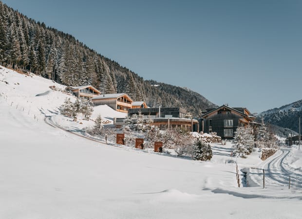 Alpines Hotelensemble liegt an einem verschneiten Hang, umgeben von winterlicher Berglandschaft und Nadelwald
