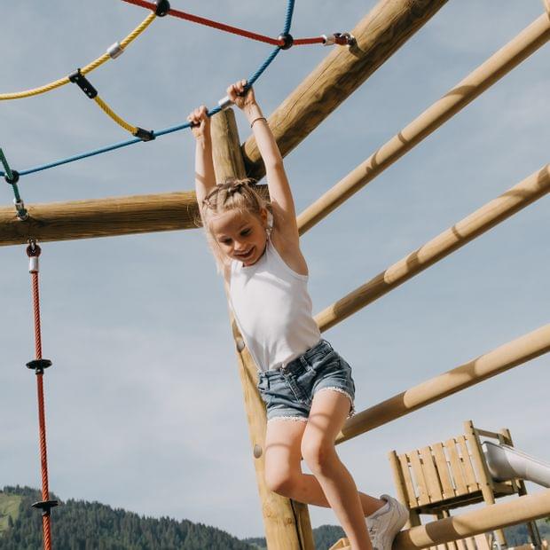 Mädchen hangelt sich an einem Kletternetz auf dem Abenteuerspielplatz