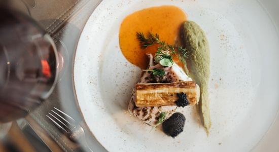 Fein angerichtetes Gourmetgericht mit Fleisch, Sauce und grünem Püree auf weißem Teller, von oben fotografiert