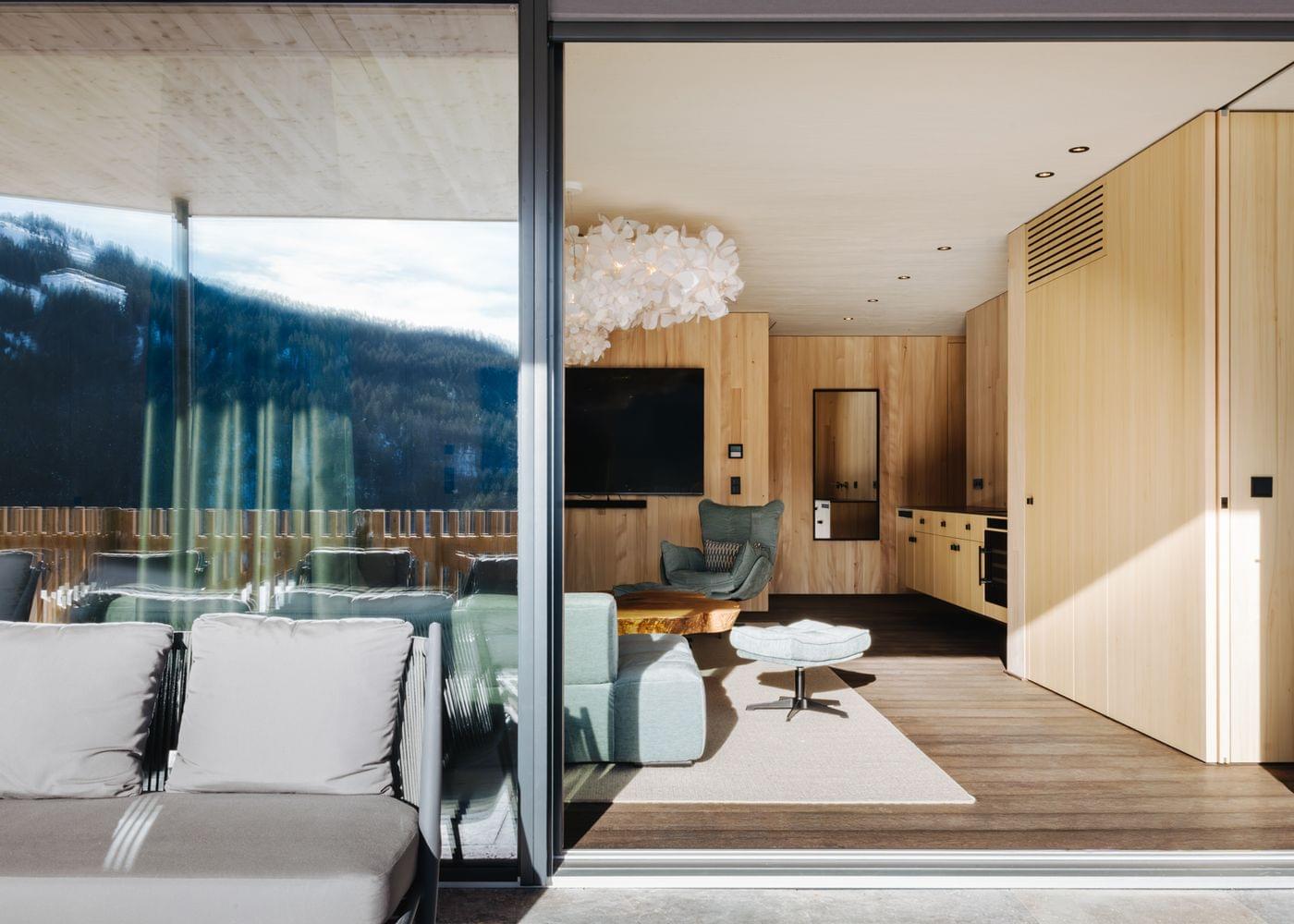 Offener Wohnbereich mit großer Glasfront, gemütlicher Sofalandschaft und Blick auf eine Terrasse mit Bergpanorama.
