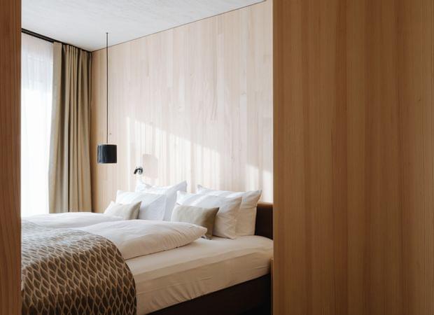 Einladendes Schlafzimmer mit großem Bett, weißen Kissen, gemustertem Überwurf und Holzverkleidung, durch eine geöffnete Tür gesehen.