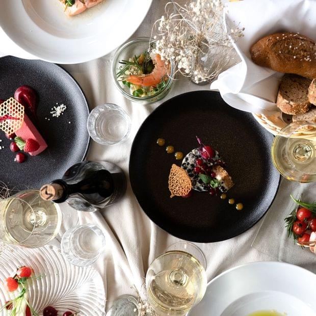 Essenstisch mit mehreren Gerichten angerichtet auf weißen und schwarzen Tellern - Torghele's Wald + Fluh