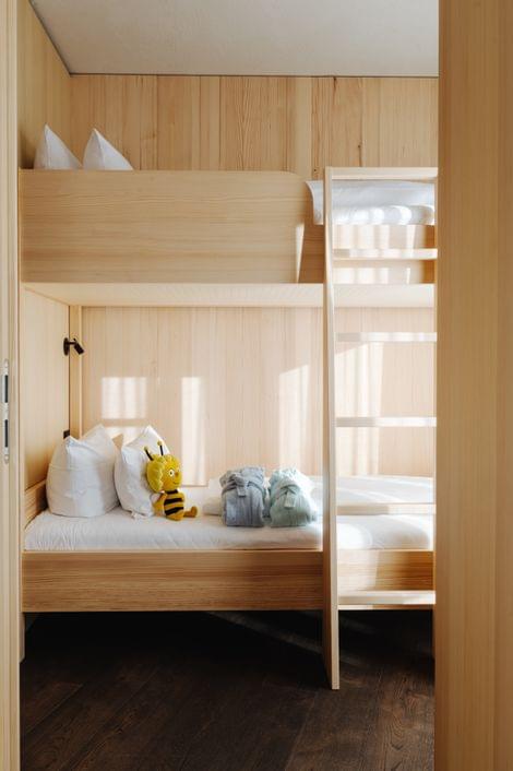 Holz-Stockbett in einem Kinderzimmer, unten mit weißen Kissen, einem gelben Kuscheltier und zwei gefalteten Bademänteln.