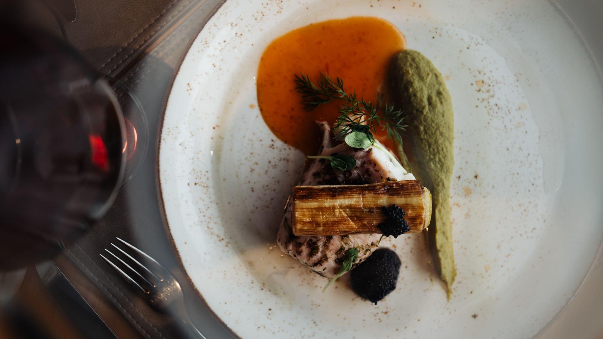Fein angerichtetes Gourmetgericht mit Fleisch, Sauce und grünem Püree auf weißem Teller, von oben fotografiert