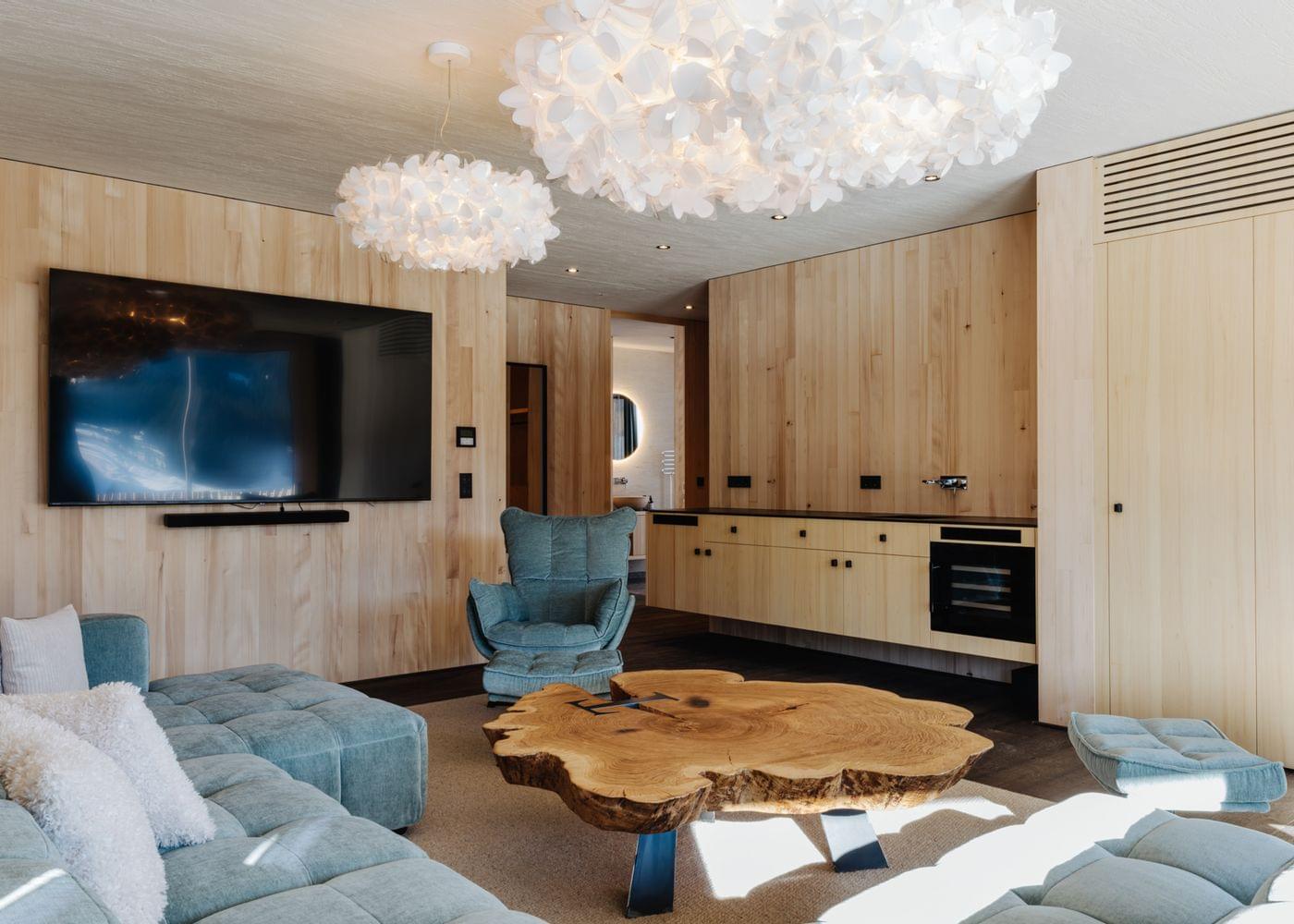 Hochwertiger Wohnraum mit großer Eckcouch, Design-Sessel, organischen Deckenleuchten und einem markanten Holzcouchtisch vor heller Holzverkleidung.