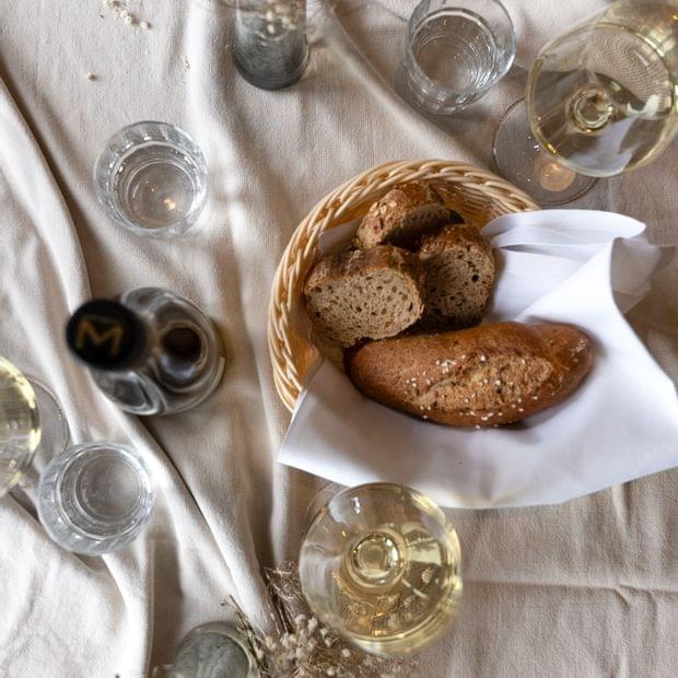 Brotkorb mit Gebäck steht neben Weinglas auf einer hellen Tischdecke - Torghele's Wald + Fluh