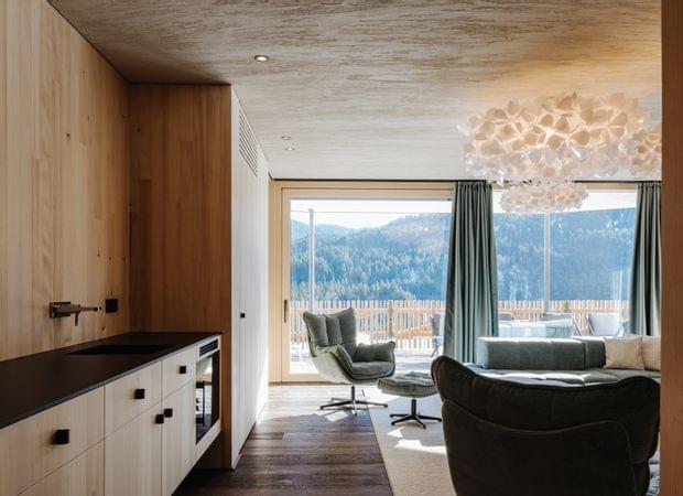 Offener Wohnbereich mit kleiner Küchenzeile, gemütlichen Sesseln und großem Fenster mit Blick auf die Berge.