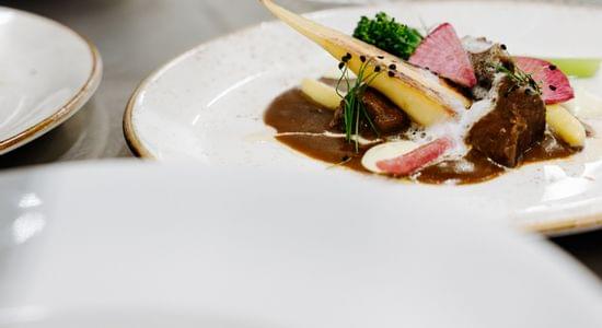 Mehrere fein angerichtete Gourmetgerichte stehen auf weiß gedecktem Tisch, eines davon scharf im Vordergrund