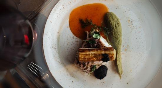 Fein angerichtetes Gourmetgericht mit Fleisch, Sauce und grünem Püree auf weißem Teller, von oben fotografiert